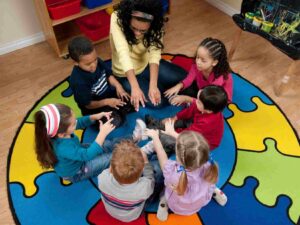 Diverse group of 6 pre-k students and teacher sitting in a circle on a colorful puzzle rug with hands reaching into center of circle for article Tucson's Private Pre-K Schools for newcomers moving to Tucson.