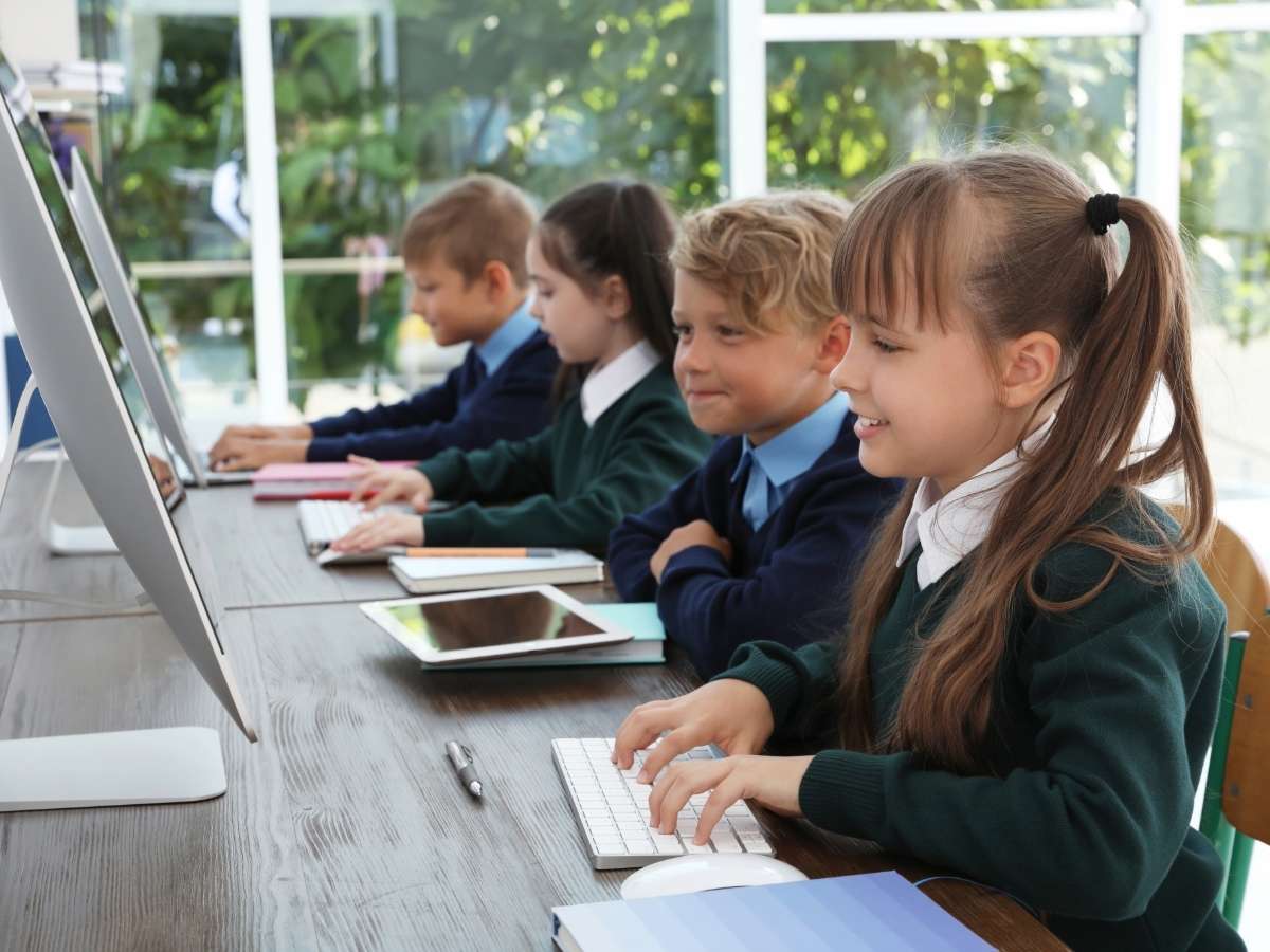 4 elementary school kids sitting in a row at a desk working on modern sleek white desktop computers for article Tucson Area Private Elementary Schools: Top Choices for 2025 Newcomers moving to Tucson.