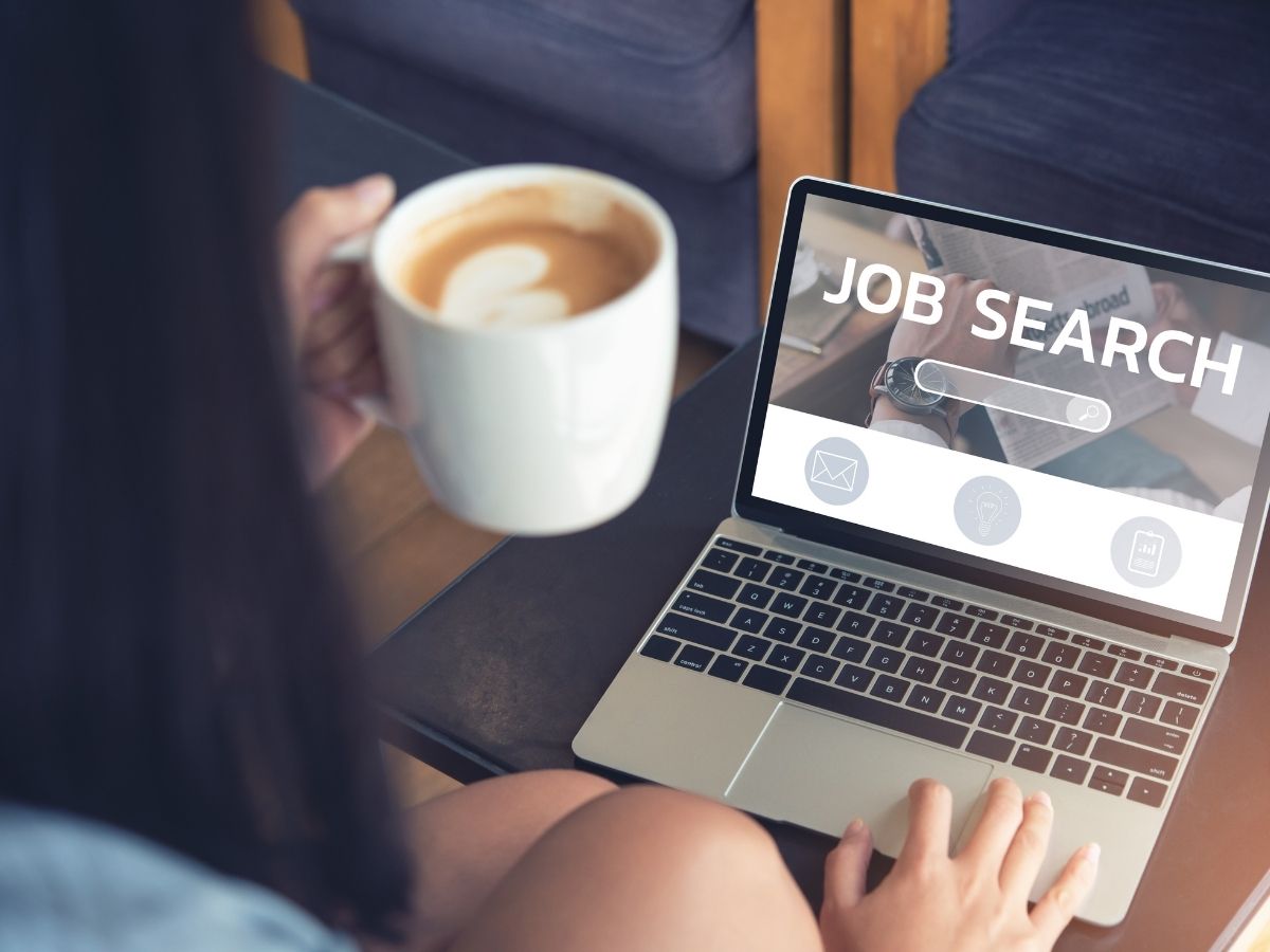 Close up of person holding cup of coffee and doing a job search on a laptop for article 5 Tips for Finding a Job in Tucson for newcomers moving to Tucson.