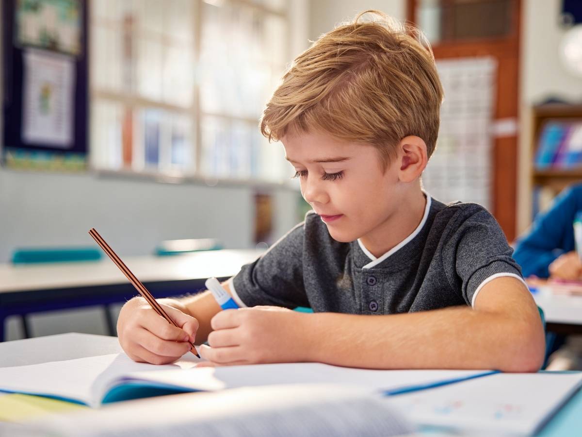School boy sitting at desk in classroom writing on paper for article Moving to Tucson with your School-Aged Child for newcomers moving to Tucson.