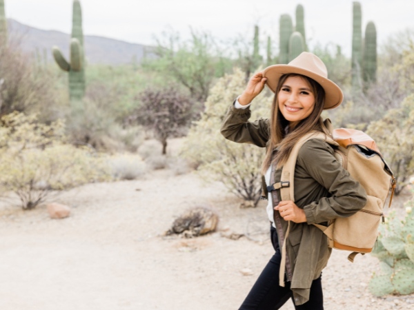 Woman with a hat and backpack on hiking in Arizona with cacti in background for article Hiking in the Valley for newcomers moving to Tucson.