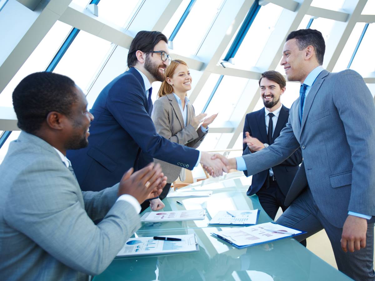 Group of 5 people at an office table - the 2 people in the center are standing and shaking hands over the table for article Is Arizona a Right to Work State - for newcomers moving to Tucson.