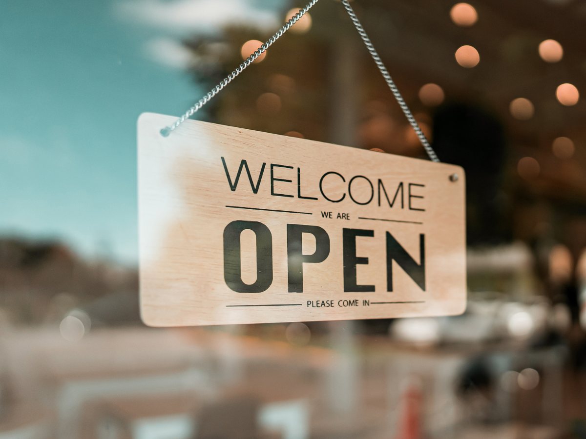 Welocme we are OPEN sign hanging in window for article 8 Best Shopping Destinations in Tucson for newcomers moving to Tucson