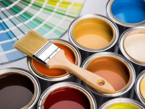 Cans of paint in all colors with brush sitting on top and color chips in background.