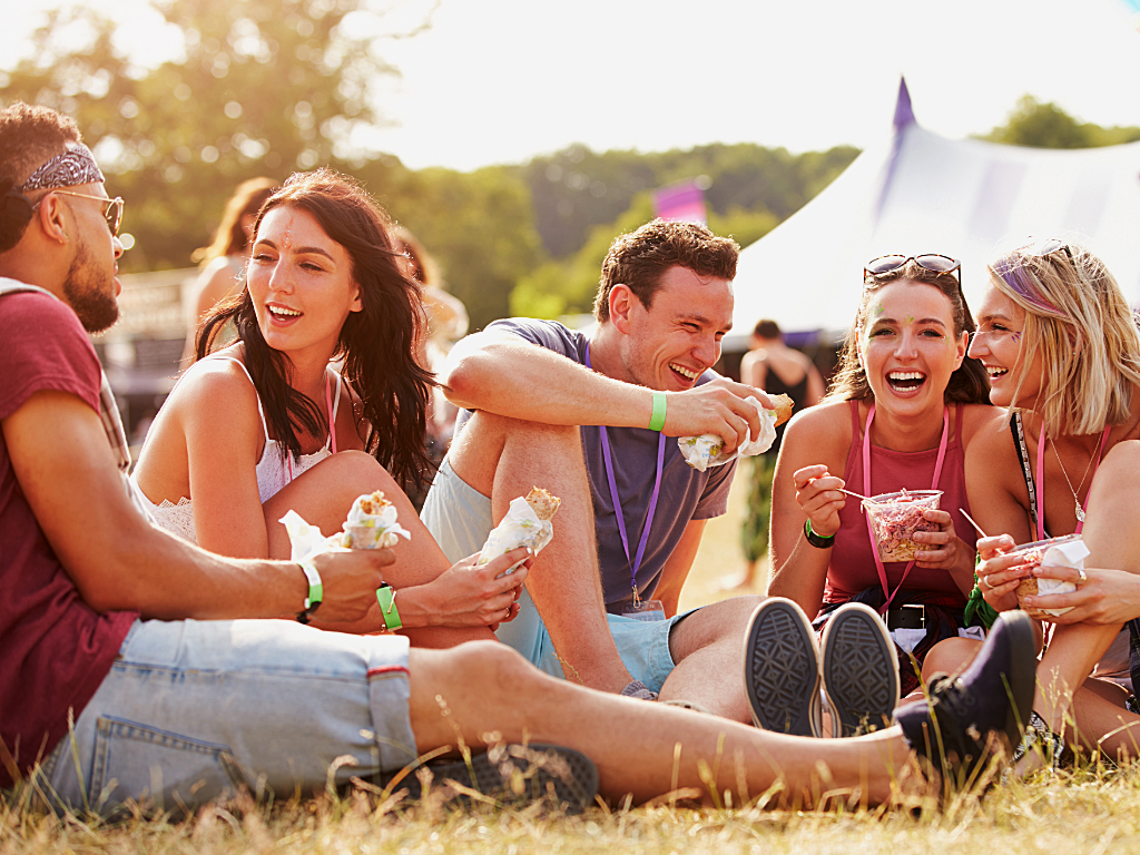 Group of young adults sitting on ground hanging out, laughing at festival.