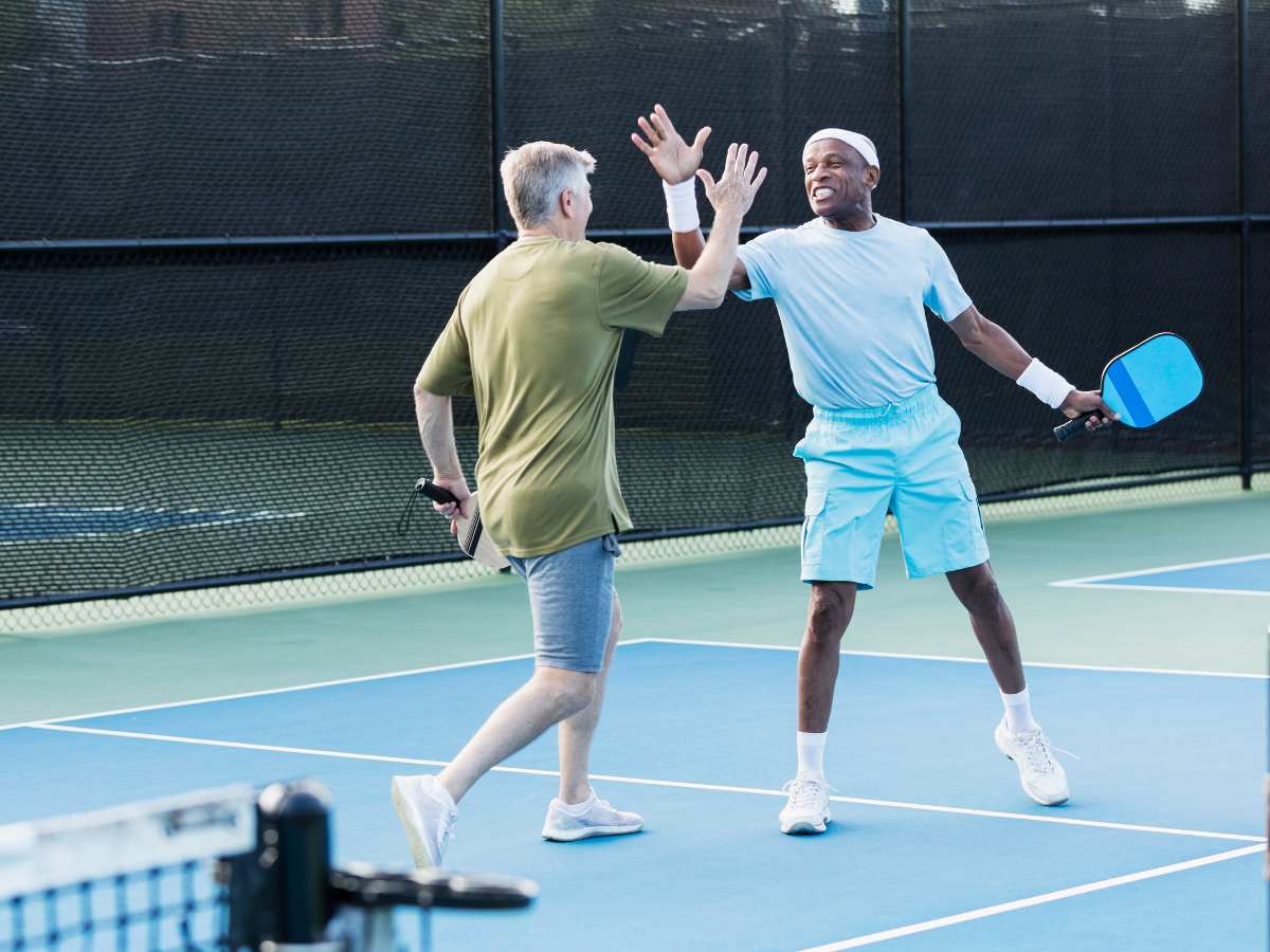 2 senior men high-fiving on a pickelball court for aricle Social Activities for Seniors in Tucson for seniors moving to Tucson.