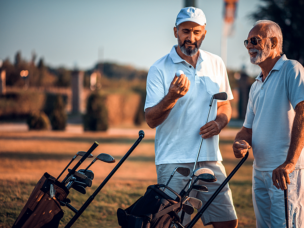 2 gentleman on golf course with rolling carts for their golf bags - looking at golf ball.