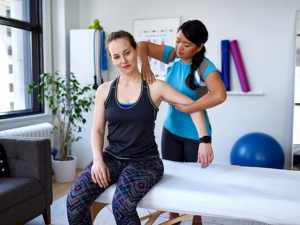 Physical therapist standing behind her seated client working on her shoulder mobility.