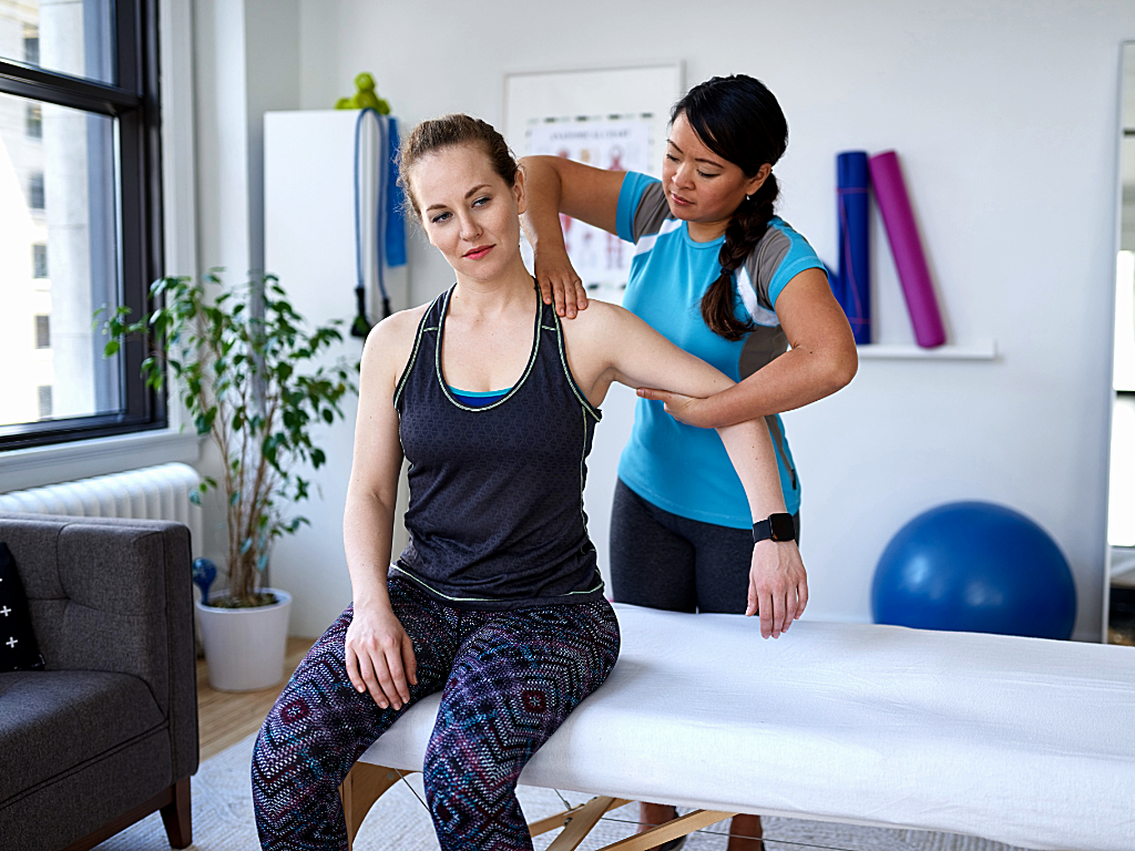 Physical therapist standing behind her seated client working on her shoulder mobility for article Physical Therapy in Tucson for newcomers moving to Tucson.