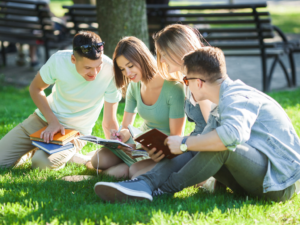 4 school kids sitting in grass studying. 10 Best College Prep High Schools in