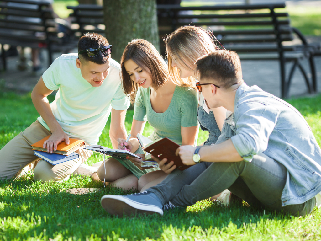 4 school kids sitting in grass studying. 10 Best College Prep High Schools in