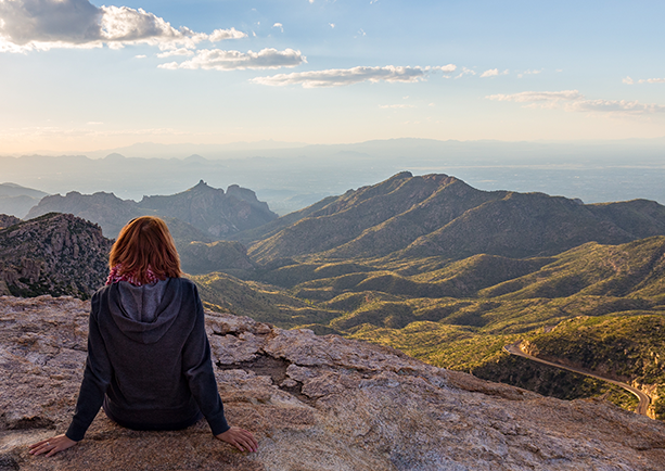 A woman staring down from the top of Mount Lemmon in Arizona while the sun starts to set.