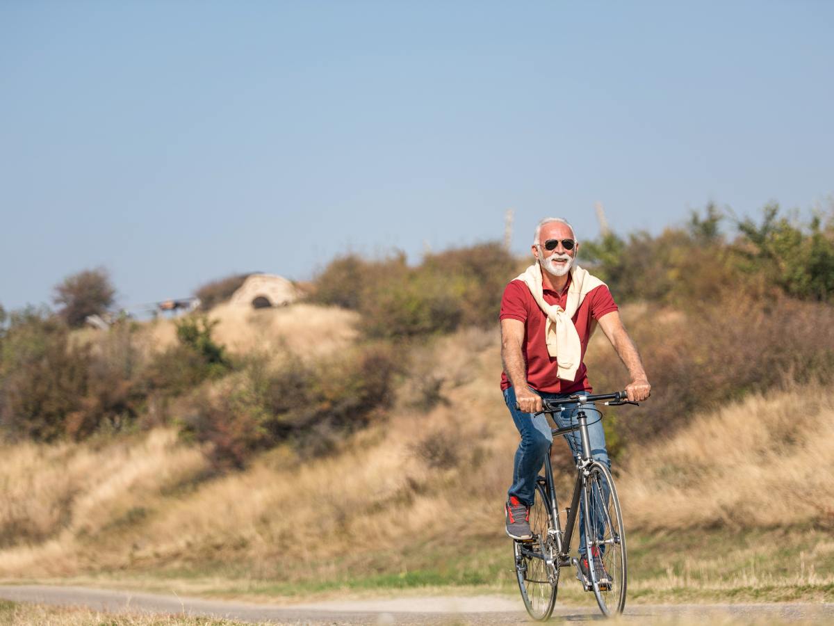 Senior male with red shirt and jeans riding a bike outdoors for article Senior Living in Tucson for newcomers moving to Tucson.