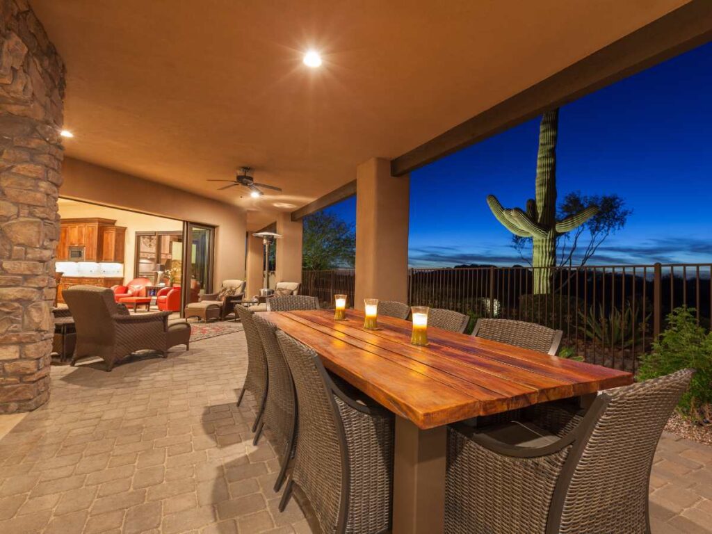 Outdoor patio of modern desert home with large wood table and patio and chairs in foreground overlooking cactus and dark blue desert sky in background for article 10 Top Homebuilders in Tucson for newcomers moving to Tucson.