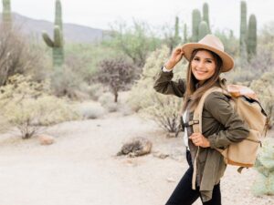 Woman with a hat and backpack on hiking in Arizona with cacti in background for article Hiking in the Valley for newcomers moving to Tucson.