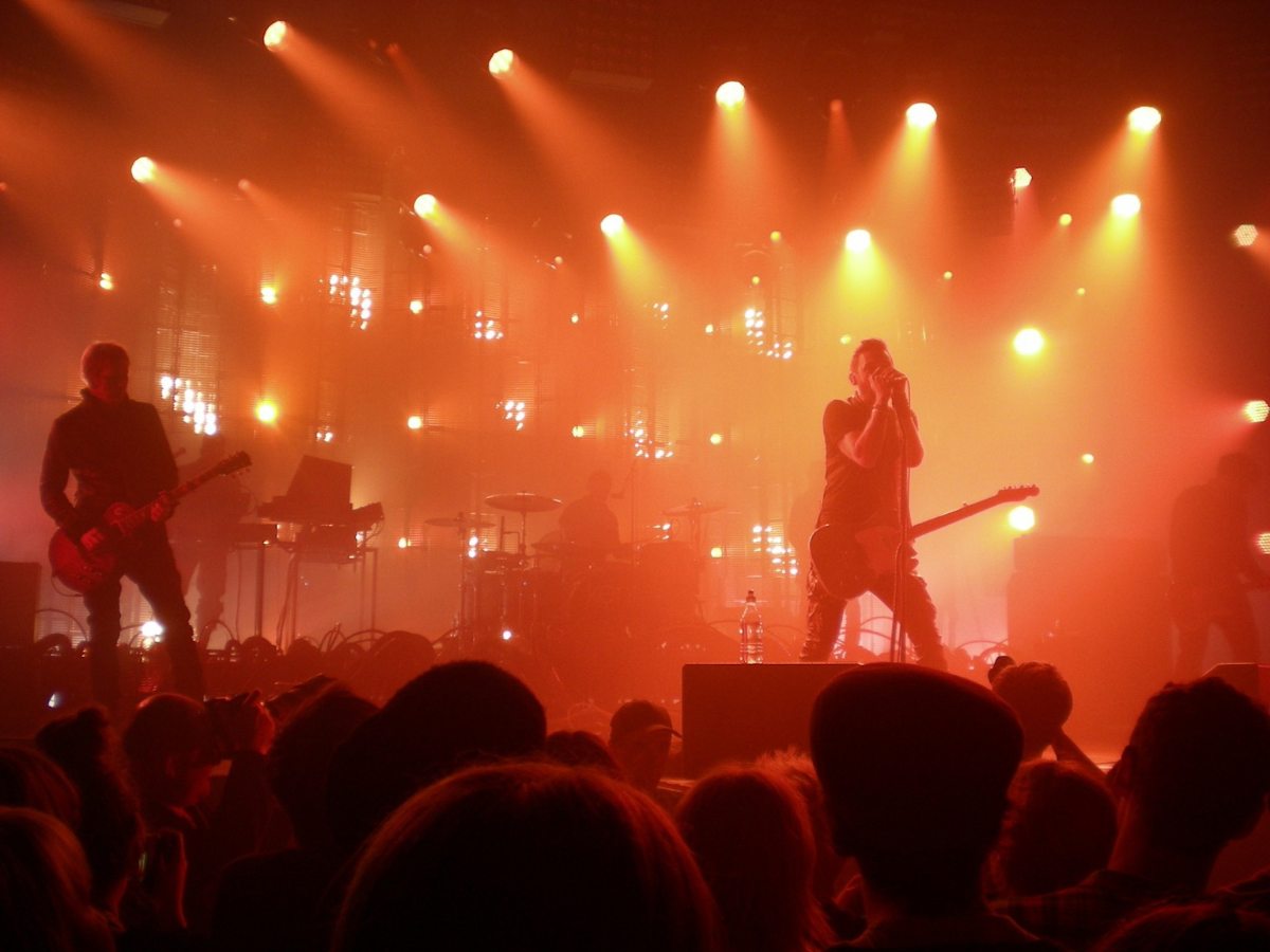 Concert with silhouettes of band members on stage in background and people standing in front of stage with yellow and orange spotlights all around the band for article Amazing Music Events and Festivals in Tucson for newcomers moving to Tucson.