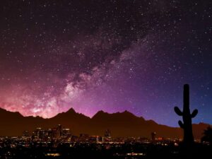 Pink and purple sky full of stars with Arizona mountains, city and cactus in the foreground for article 6 Best Stargazing Spots in Tucson for newcomers moving to Tucson.